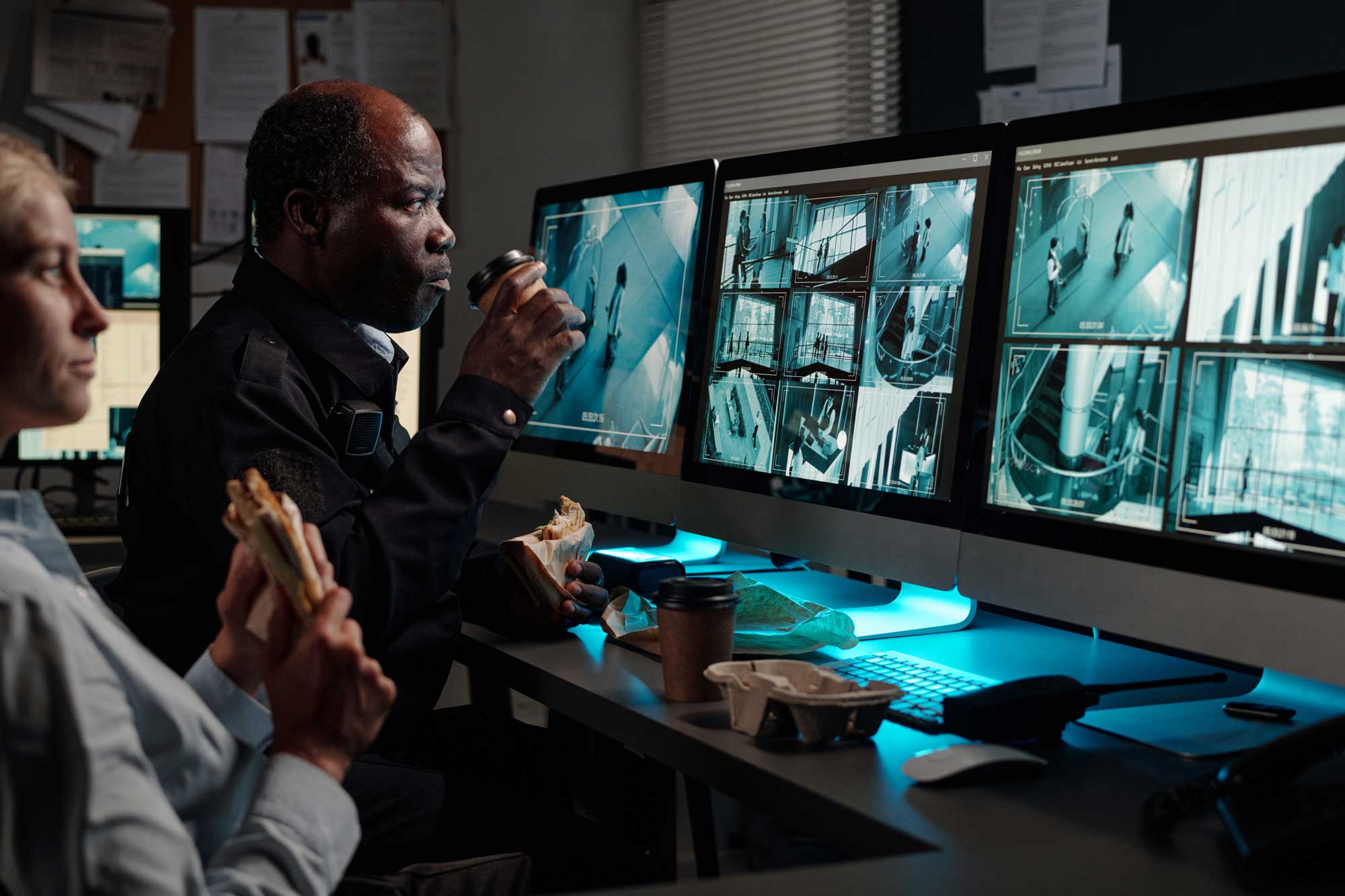 Two security guards enjoy lunch while watching CCTV monitors.